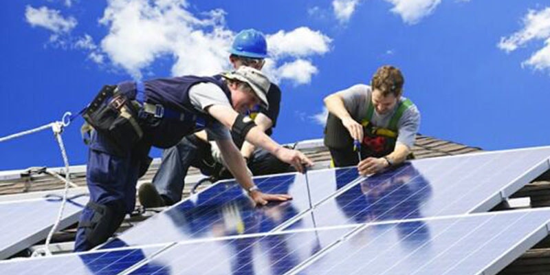 three solar installers installing solar panels on a tiled roof