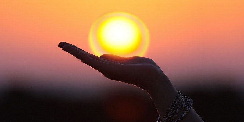 hand appearing to holding sun during beautiful sunset