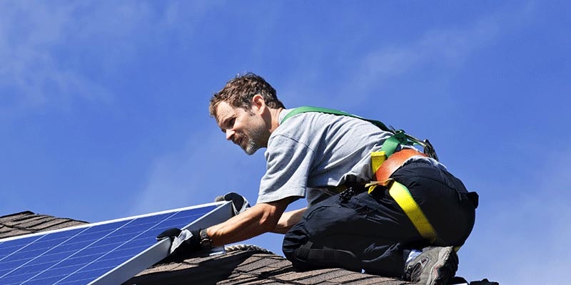 solar installer in harness mounting solar panel on tiled roof
