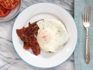 Over easy egg on a plate with bacon and broiled tomatoes.