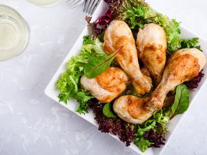 Roast chicken legs on white plate over light gray table