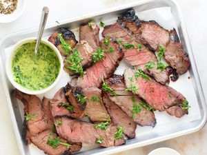 grilled chuck roast sliced on a tray with chimichurri