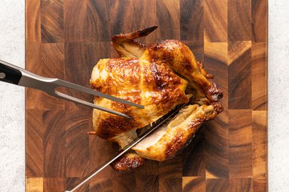 whole roasted chicken being carved on cutting board, knife cutting into separate leg from breast