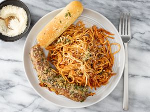 plate with baked crispy spaghetti, a breadstick, and italian sausage