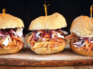 Three barbecued pulled chicken sandwiches on a cutting board