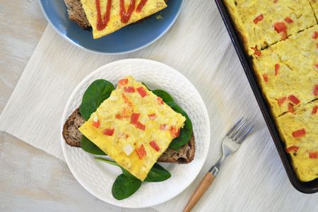 Sheet pan eggs, slice served on a plate over toast and spinach