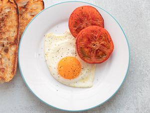 Sunny-side up egg on a plate with charred tomatoes.