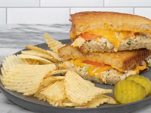 tuna melt sandwich on a plate with chips and pickles
