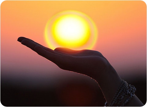 hand appearing to holding sun during beautiful sunset