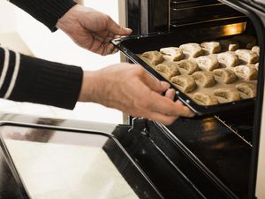 Close-up of a man putting baking tray of vanilla crescents in oven for baking, Munich, Bavaria, Germany