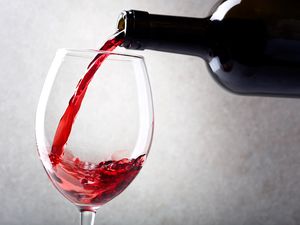 Red wine is poured into a glass from a bottle. Light background.